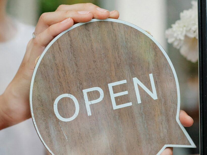 Henkilö asettaa ulko-oveen open -kylttiä.