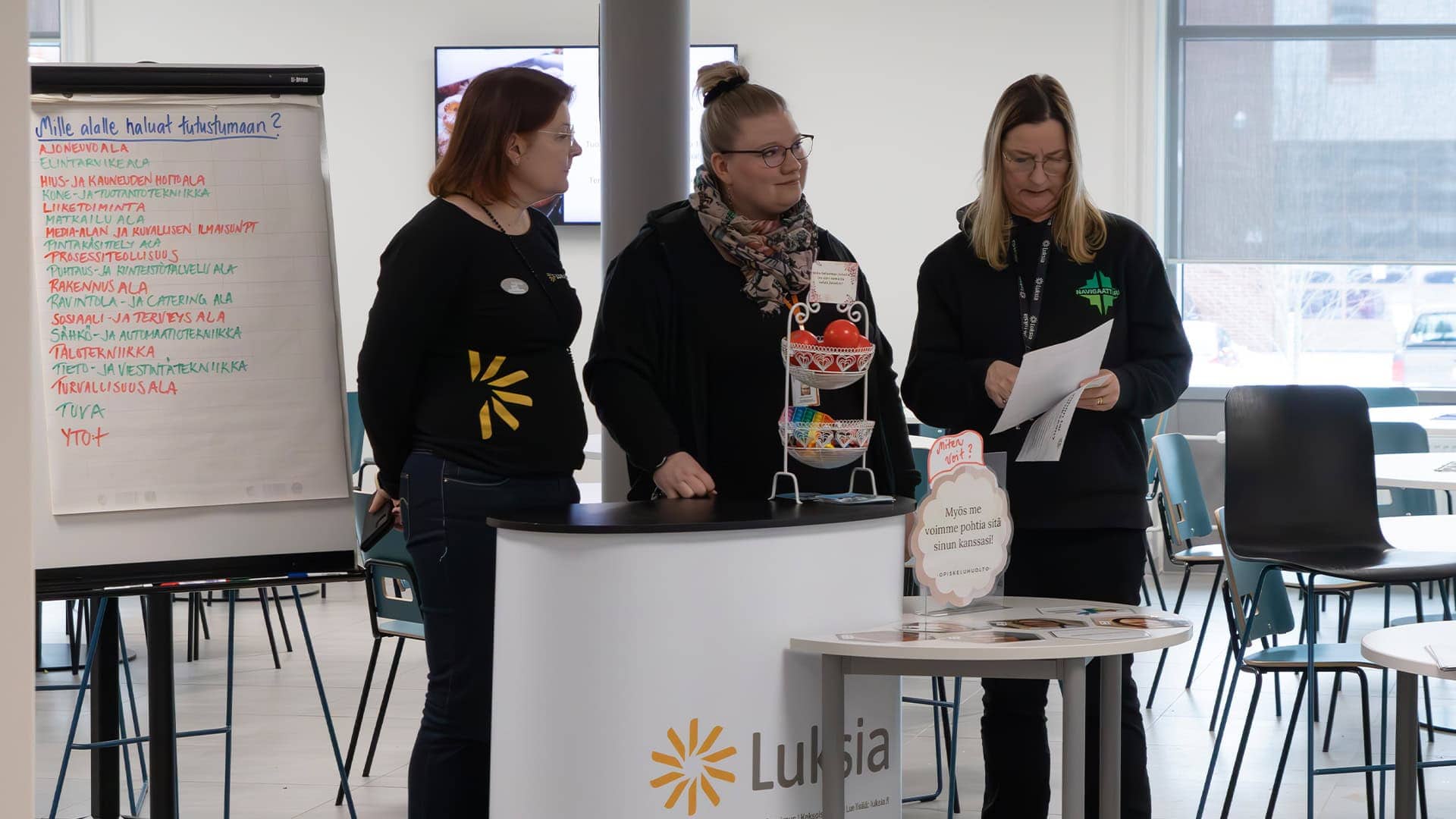 Kolme ihmistä seisoo fläppitaulun edessä ja tutkii asiakirjaa.