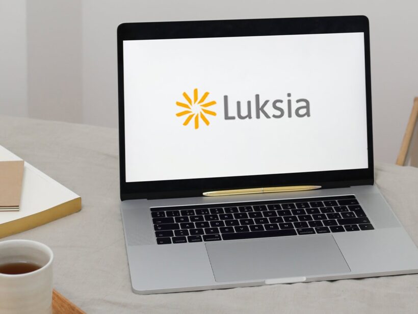 Pöydällä on kannettava, jossa on näytöllä Luksian logo, kirjoja sekä teekuppi.