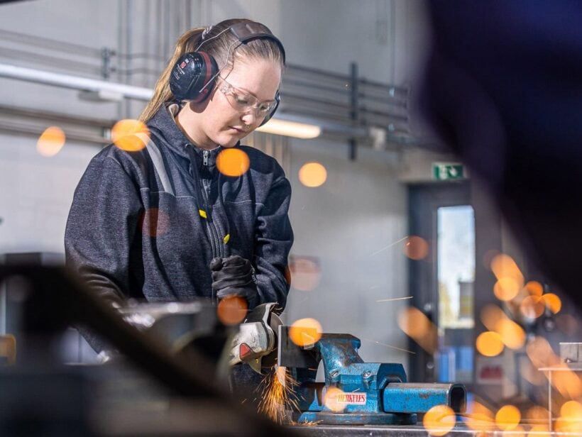 Henkilö tummassa haalarissa työn ääressä konepajalla.