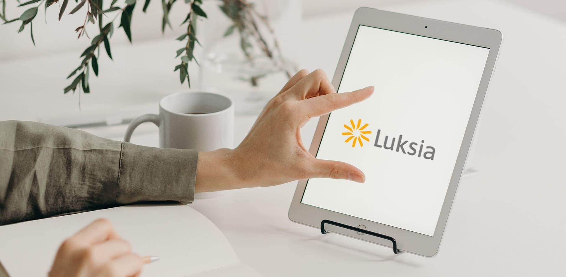 Tabletin näytöllä on Luksian logo. Sormet skaalaavat logoa suuremmaksi.