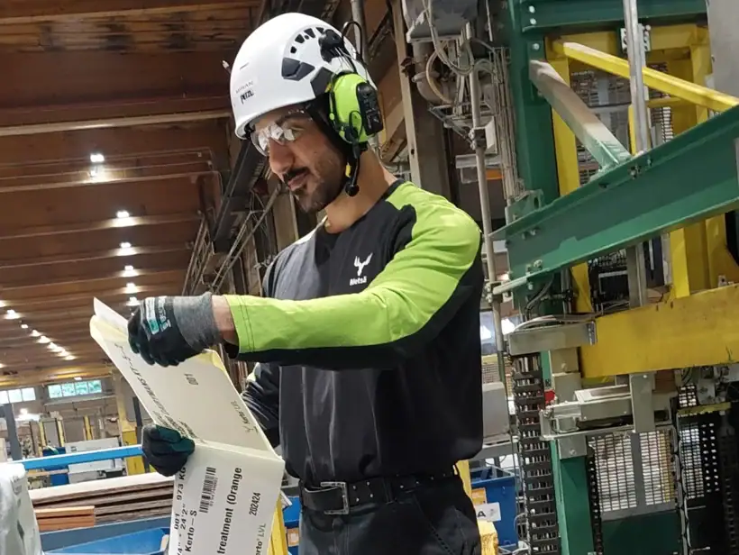 Henkilö seisoo pakkauslinjan edessä ja pitää kädessään pakkausmateriaalia.