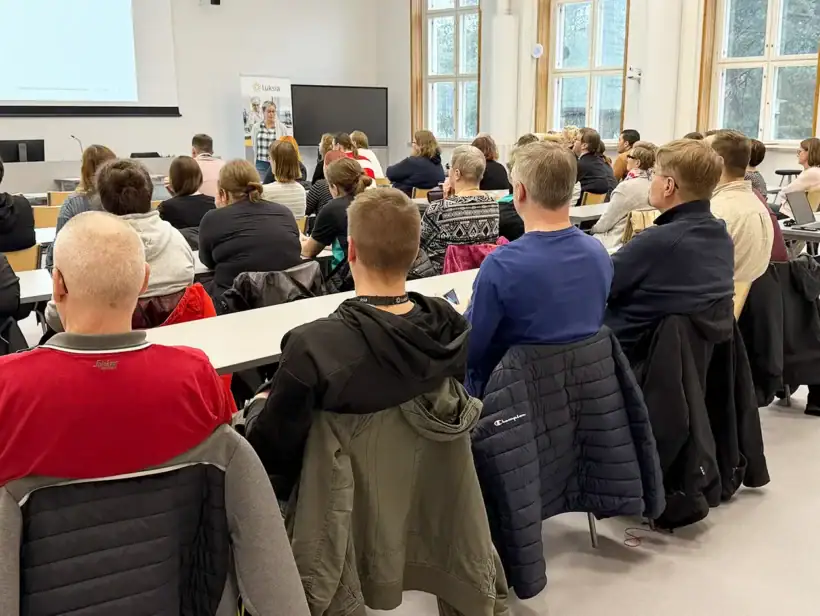 Luentosalissa joukko ihmisiä kuuntelee luennoitsijaa, joka seisoo yleisön edessä.