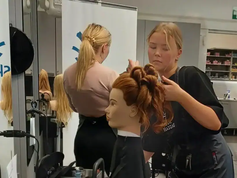 Henkilö tummassa asussa tekee kampausta kampauspäälle.