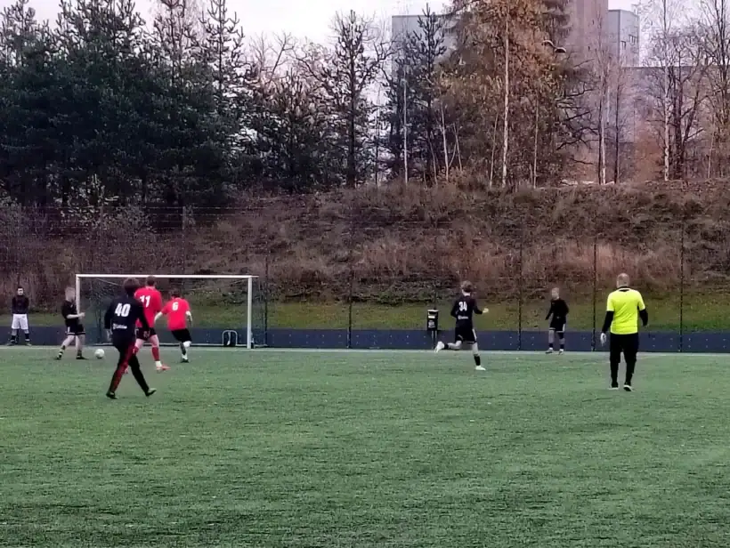 Vihreällä jalkapallokentällä pelaajia punaisissa, mustissa ja keltaisissa asuissa.