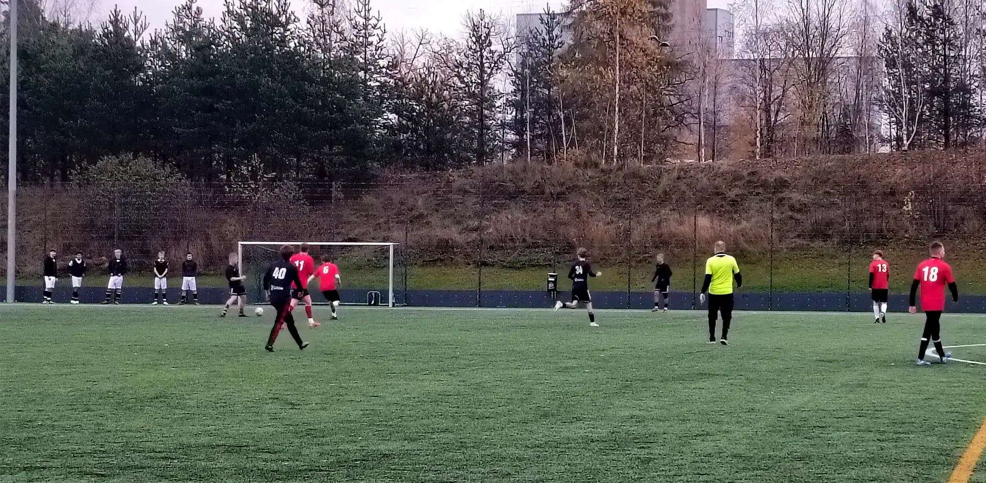Vihreällä jalkapallokentällä pelaajia punaisissa, mustissa ja keltaisissa asuissa.