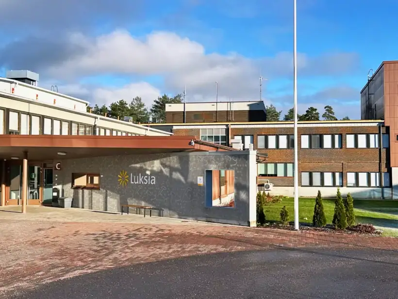 Kampusrakennus kuvattuna parkkipaikalta. Taustalla sininen taivas ja auringonvalo.