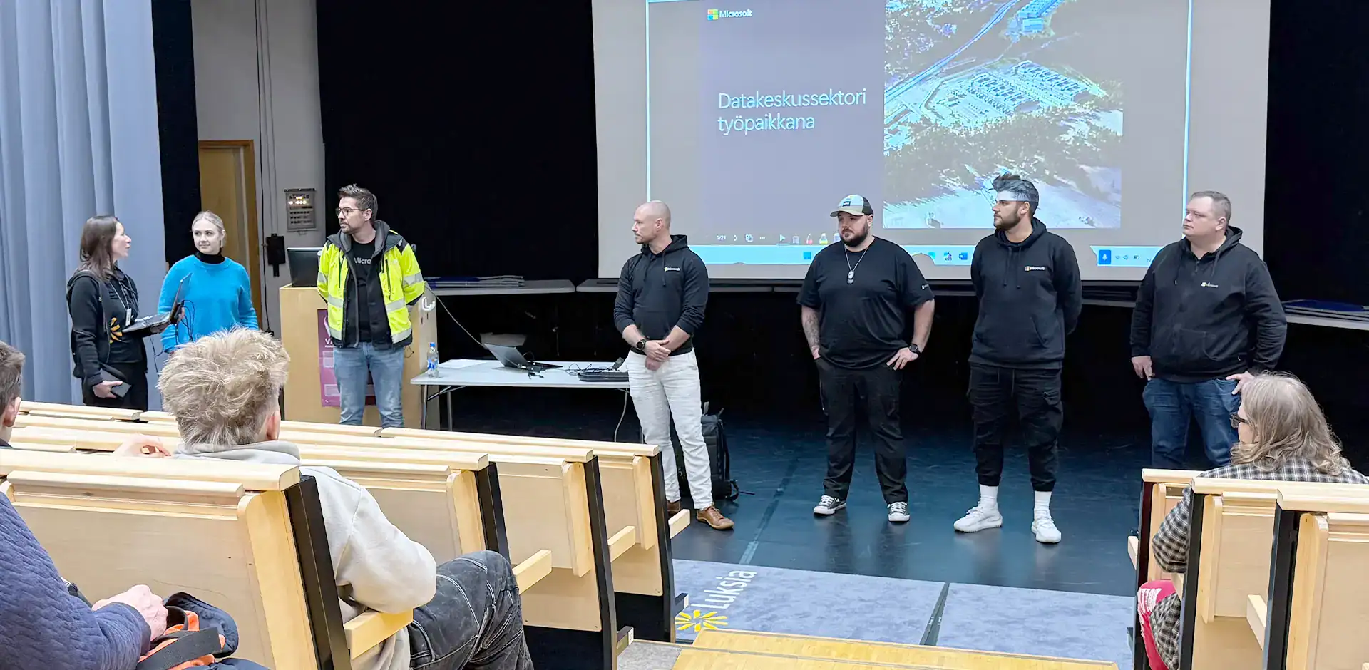 Luentosalin esiintymislavalla joukko ihmisiä.