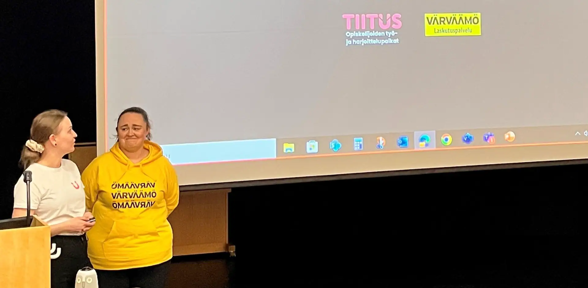 Kaksi henkilöä esittelee työtään lavalla. Lavalle on heijastettu työpaikkojen nimet.