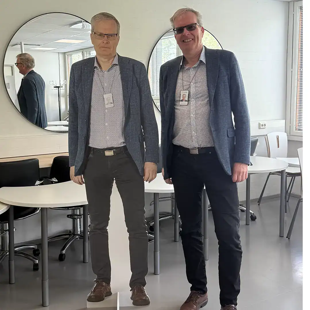 Henkilö sinisessä pikkutakissa seisoo oman pahvikuvansa vieressä.