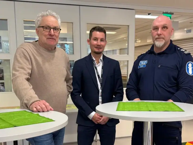 Kolme henkilöä ruokalamiljöössä. Yksi henkilöistä on poliisin virka-asussa.
