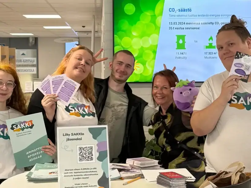 Viisi iloista henkilöä rivissä ja poseeraa kameralle.