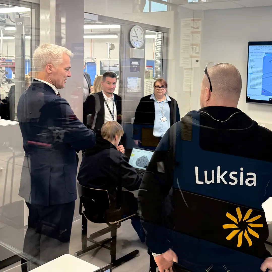 Ihmisiä tummissa vaatteissa seuraa luokkahuoneessa opetusta.