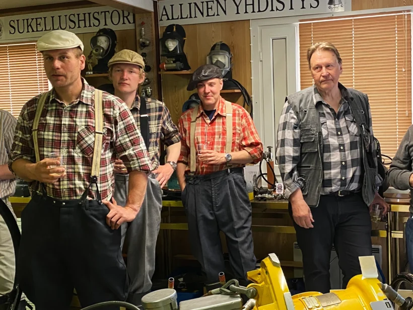 Kuusi ihmistä seisoo kuvassa. Neljällä on päällään ruutupaidat. Kaikilla on kädessä kuohuviinilasi.