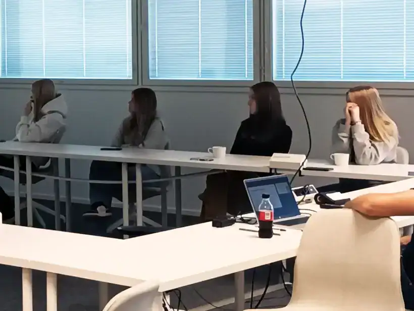 Opiskelijat istuvat pöydän ääressä ja katsovat esitystä, joka heijastetaan seinälle.