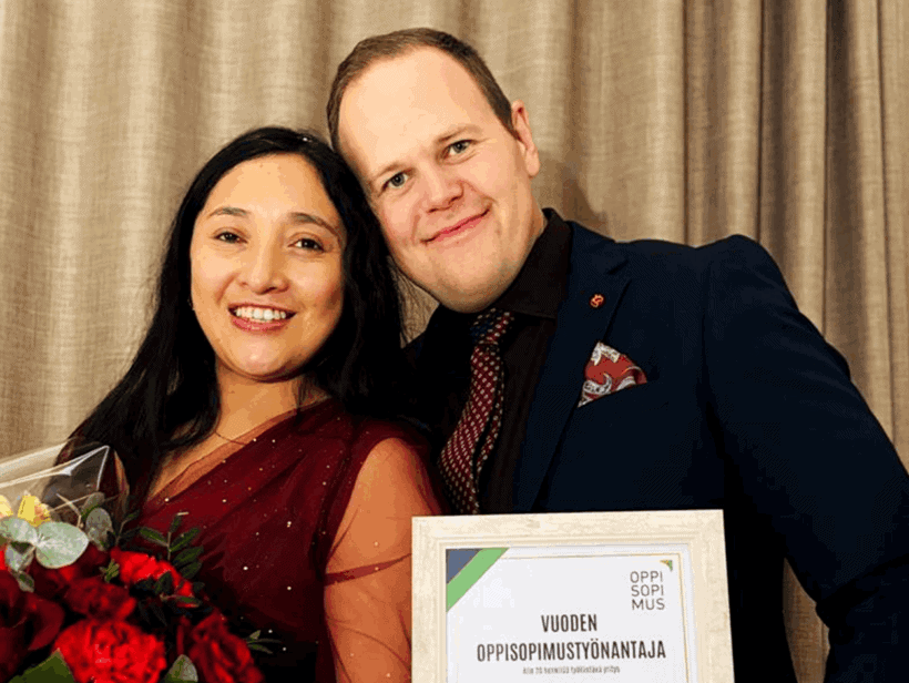 Kaksi henkilöä juhlivat voittoa. Toisella tumma puku toisella viininpunainen mekko.