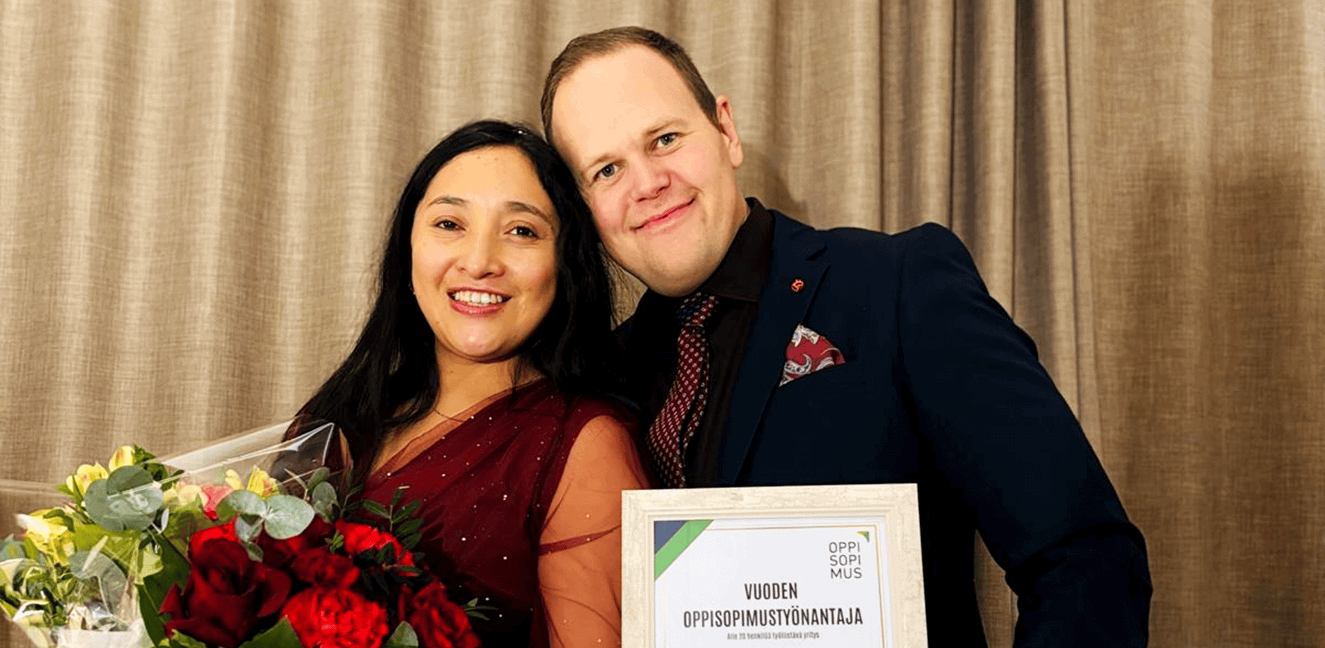 Kaksi henkilöä juhlivat voittoa. Toisella tumma puku toisella viininpunainen mekko.