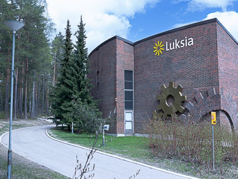 Ruskeatiilinen rakennus, sininen taivas ja vihreää metsää.