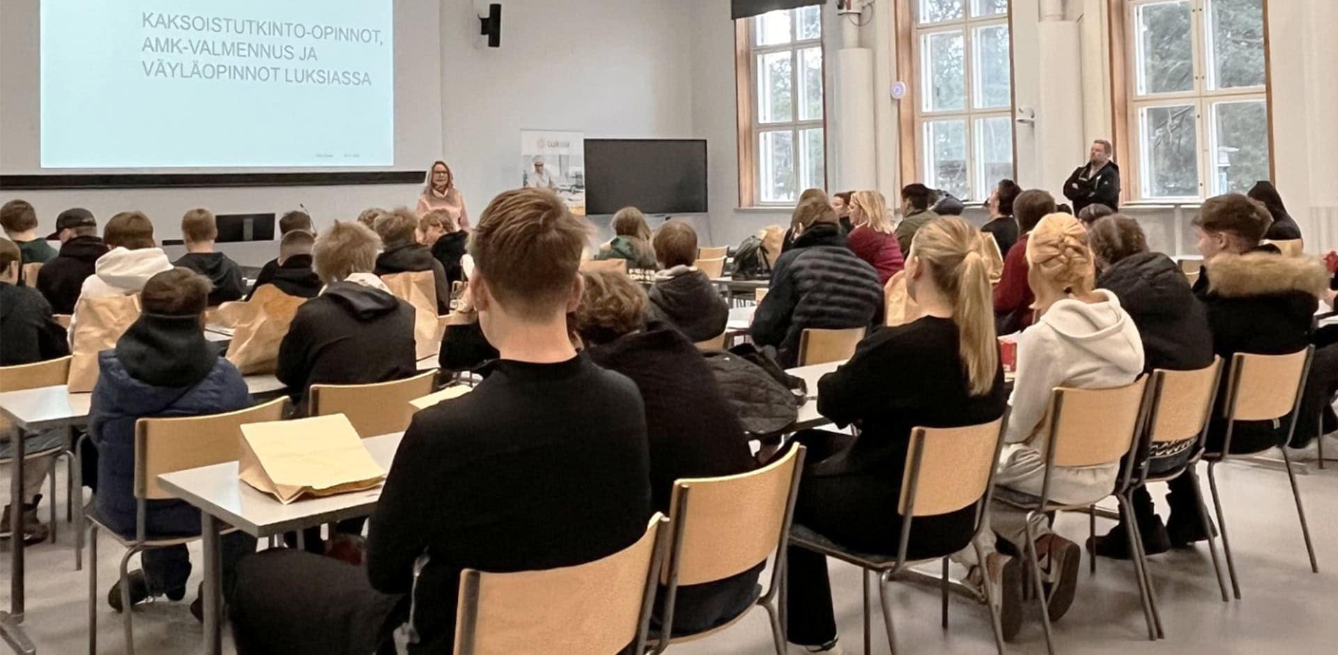 Ihmisiä luentosalissa, jossa luento käynnissä.