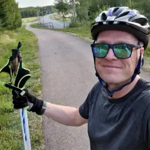 Henkilö sauvat toisessa kädessä, aurinkolasit ja pyöräilykypärä päässä.