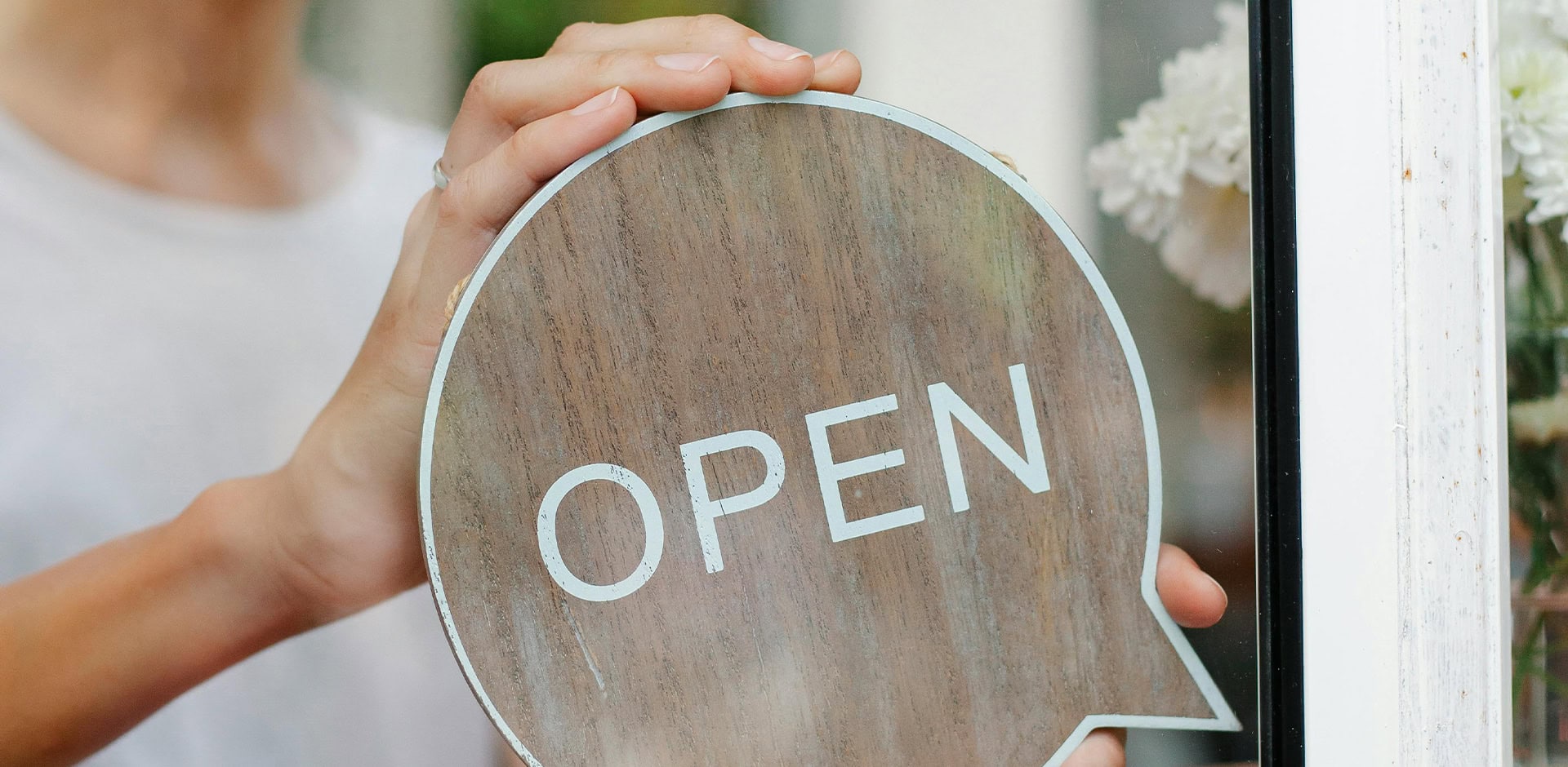 Henkilö asettaa ulko-oveen open -kylttiä.
