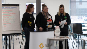 Kolme ihmistä seisoo fläppitaulun edessä ja tutkii asiakirjaa.