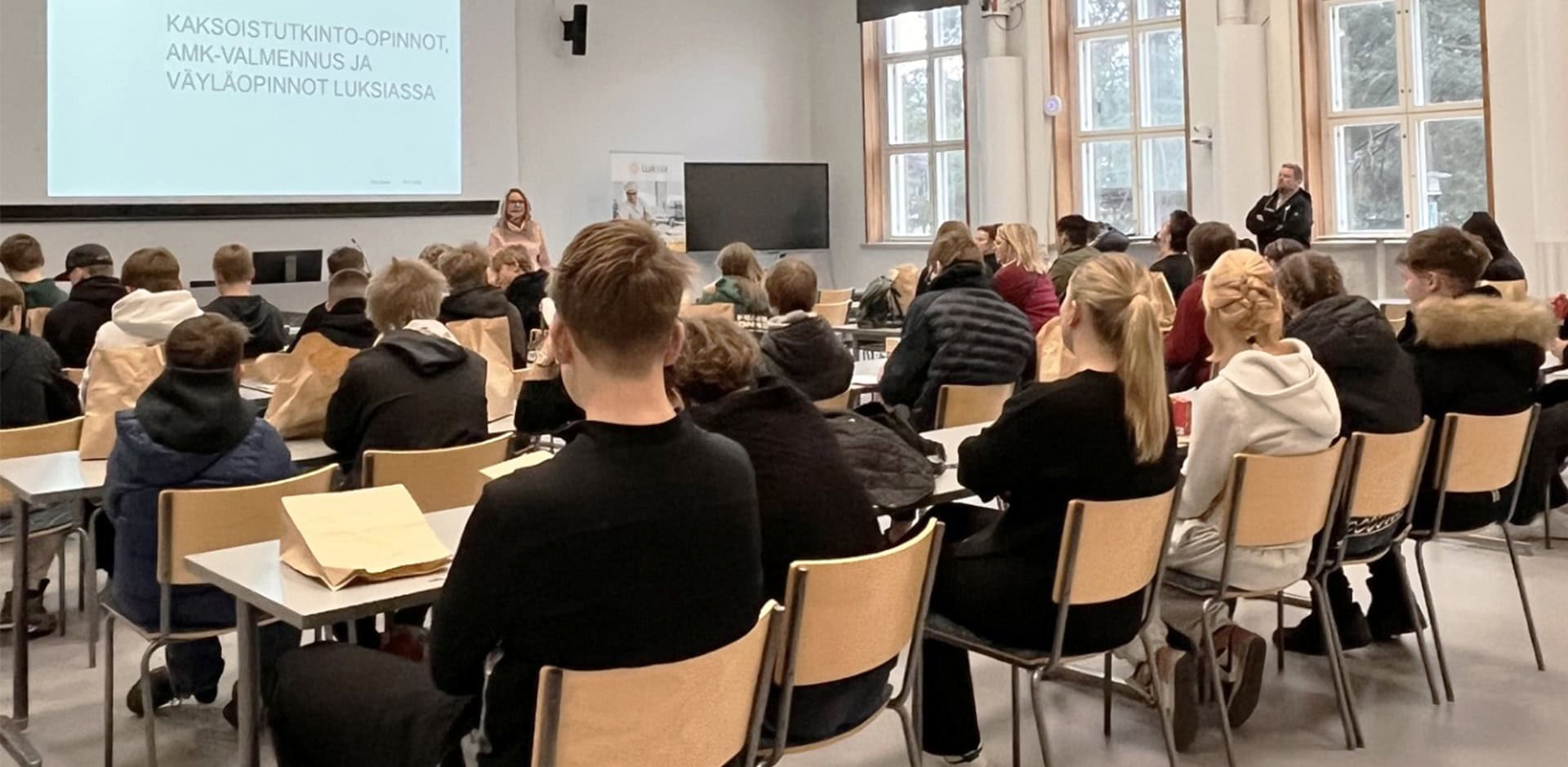 Ihmisiä luentosalissa, jossa luento käynnissä.