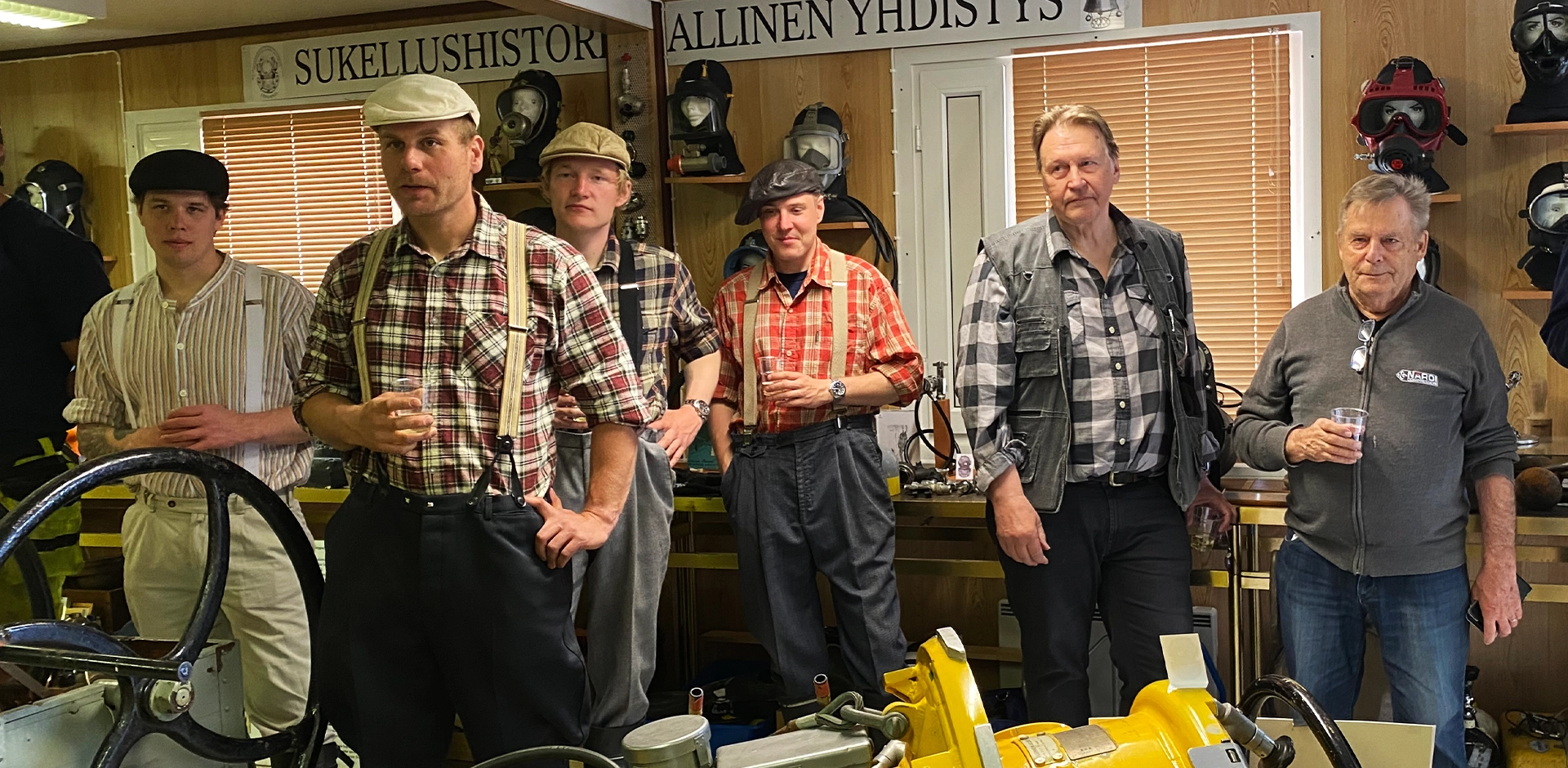 Kuusi ihmistä seisoo kuvassa. Neljällä on päällään ruutupaidat. Kaikilla on kädessä kuohuviinilasi.