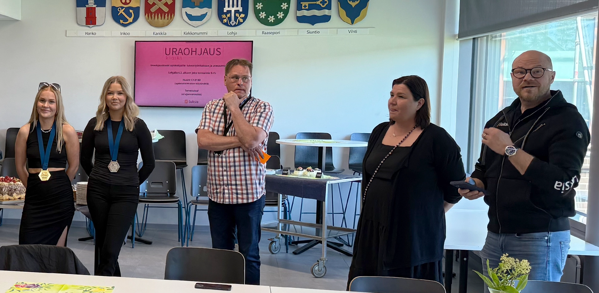 Viisi ihmistä seisoo rivissä ja keskustelee.