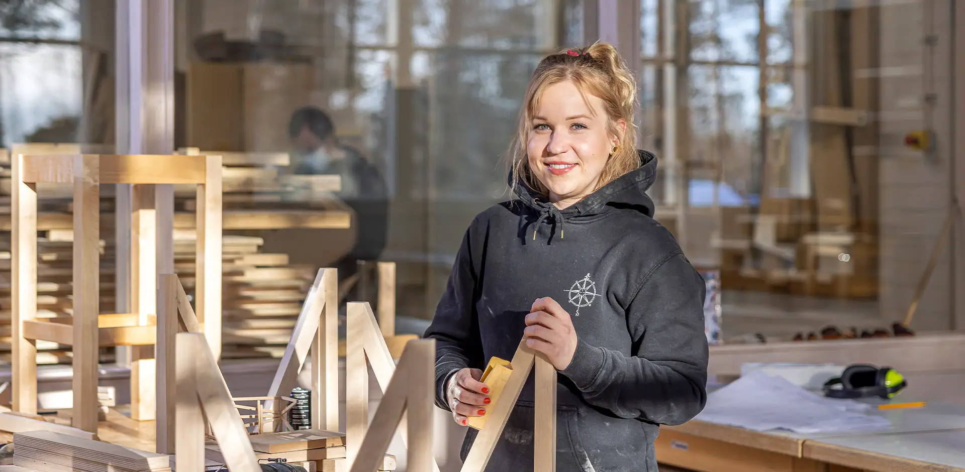 Puutyöverstaalla henkilö mustassa hupparissa.