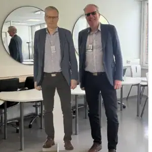 Henkilö sinisessä pikkutakissa seisoo oman pahvikuvansa vieressä.