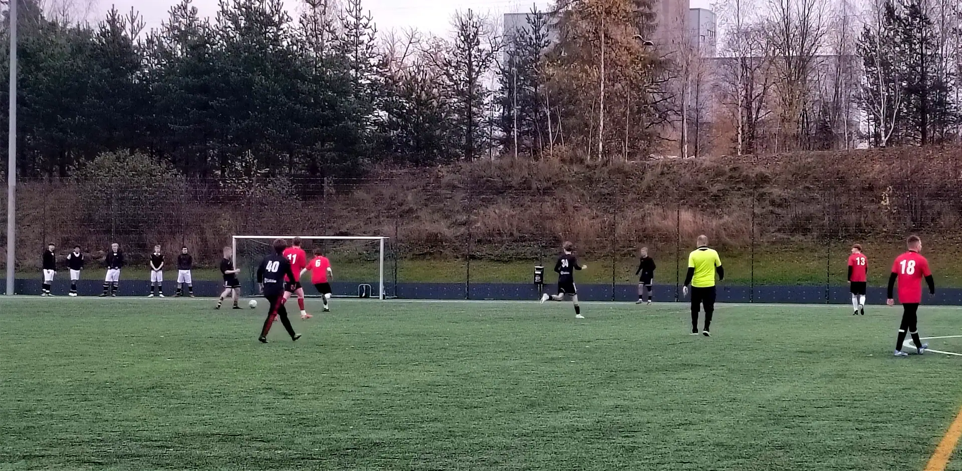 Vihreällä jalkapallokentällä pelaajia punaisissa, mustissa ja keltaisissa asuissa.