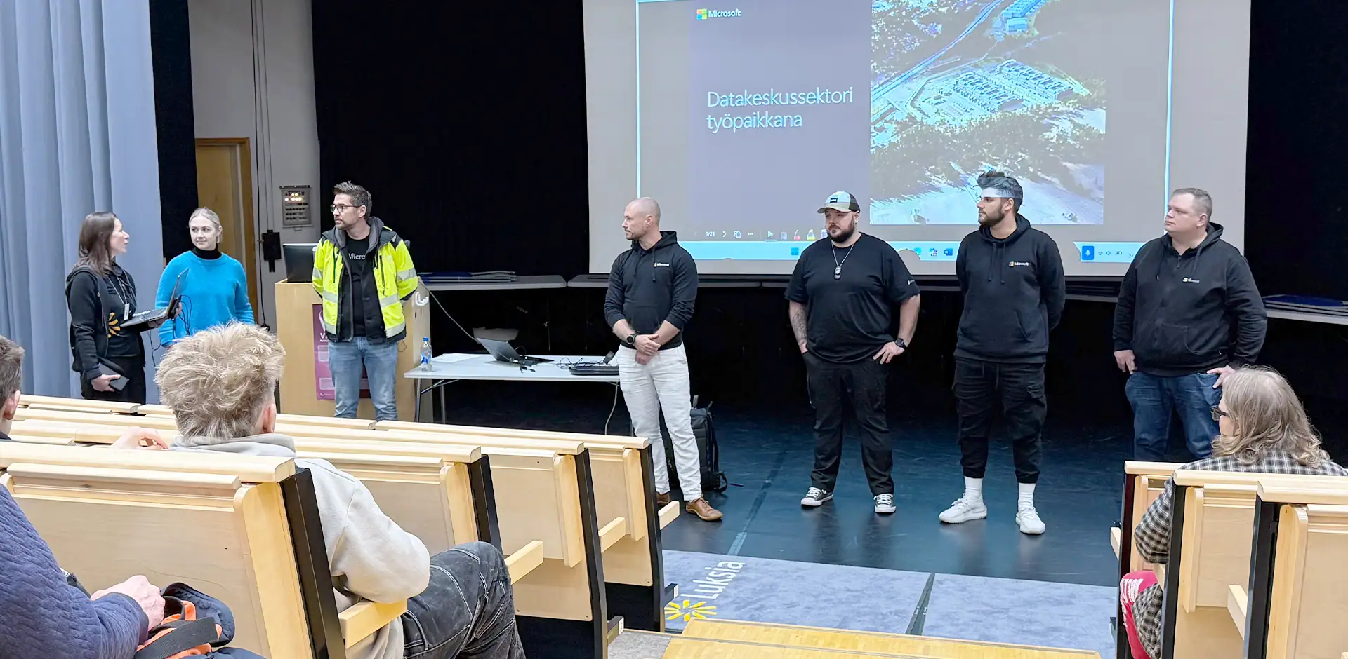 Luentosalin esiintymislavalla joukko ihmisiä.