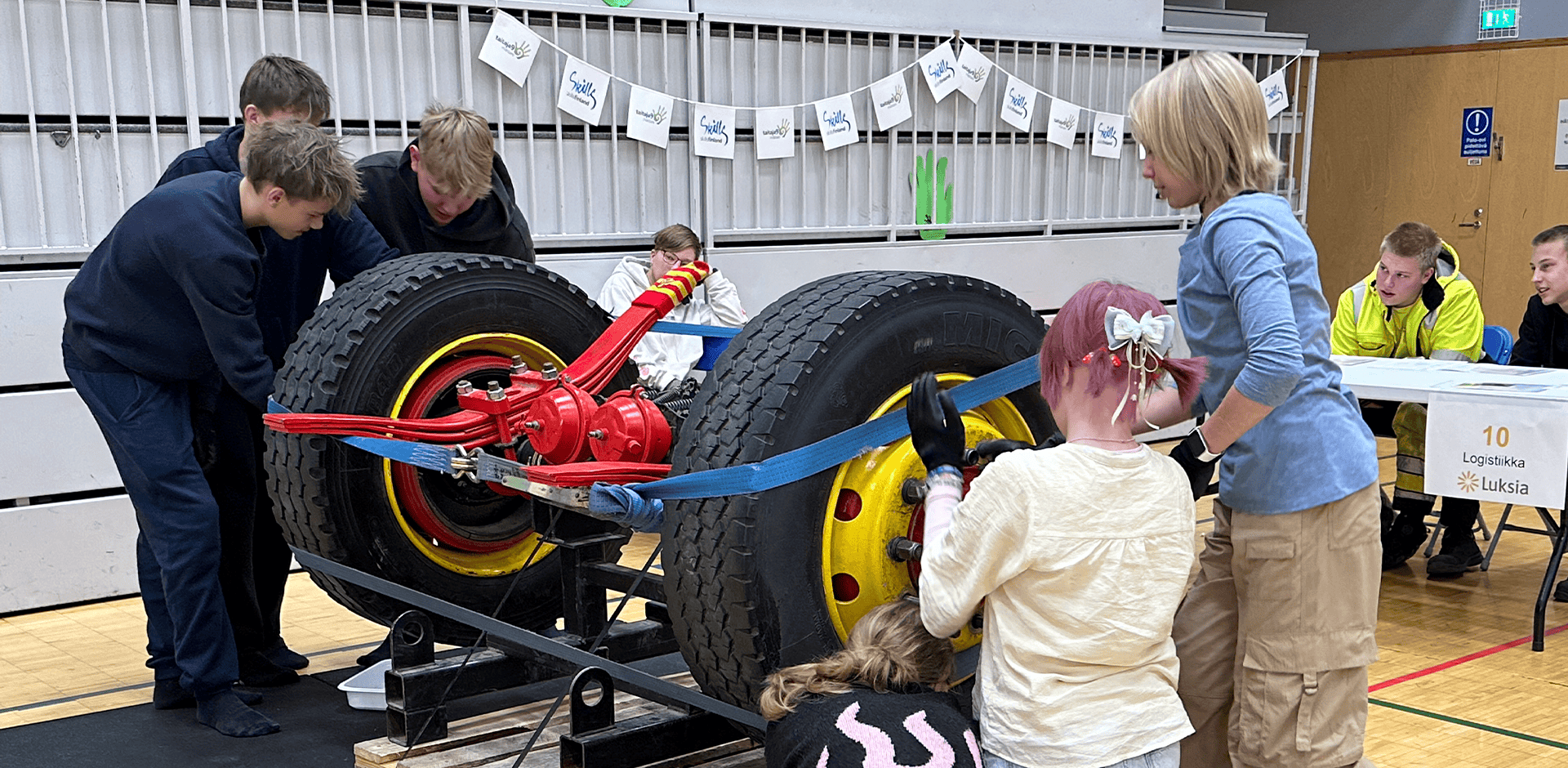 Nuoria ihmisiä tutkii isoja auton pyöriä.