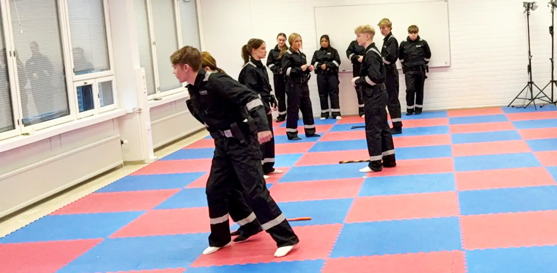 Turvallisuusalan opiskelijat harjoitustilassa tummat työasut päällään.