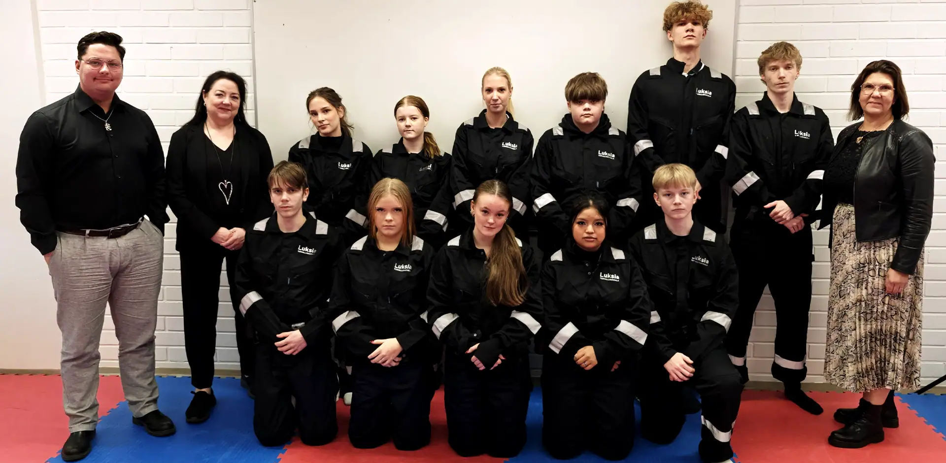 Ryhmä ihmisiä tummissa vaatteissa poseeraa kameralle.