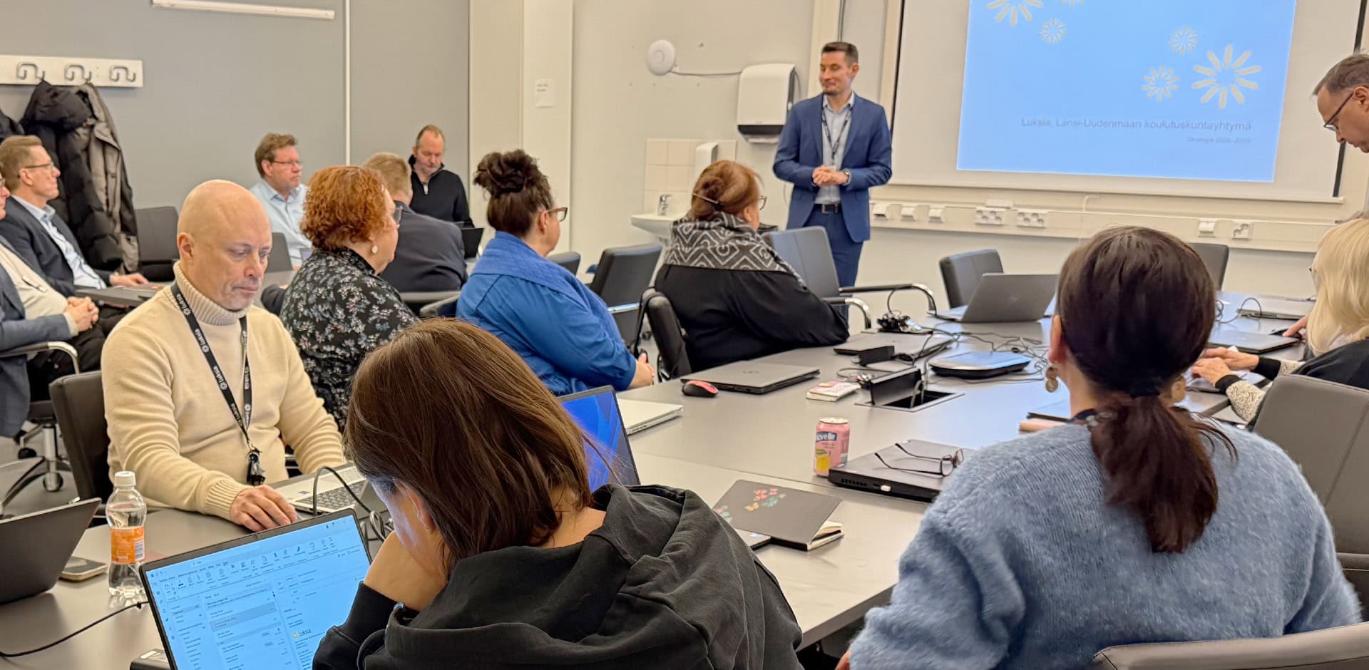 Luokkatilassa henkilöitä kuuntelemassa esitystä.