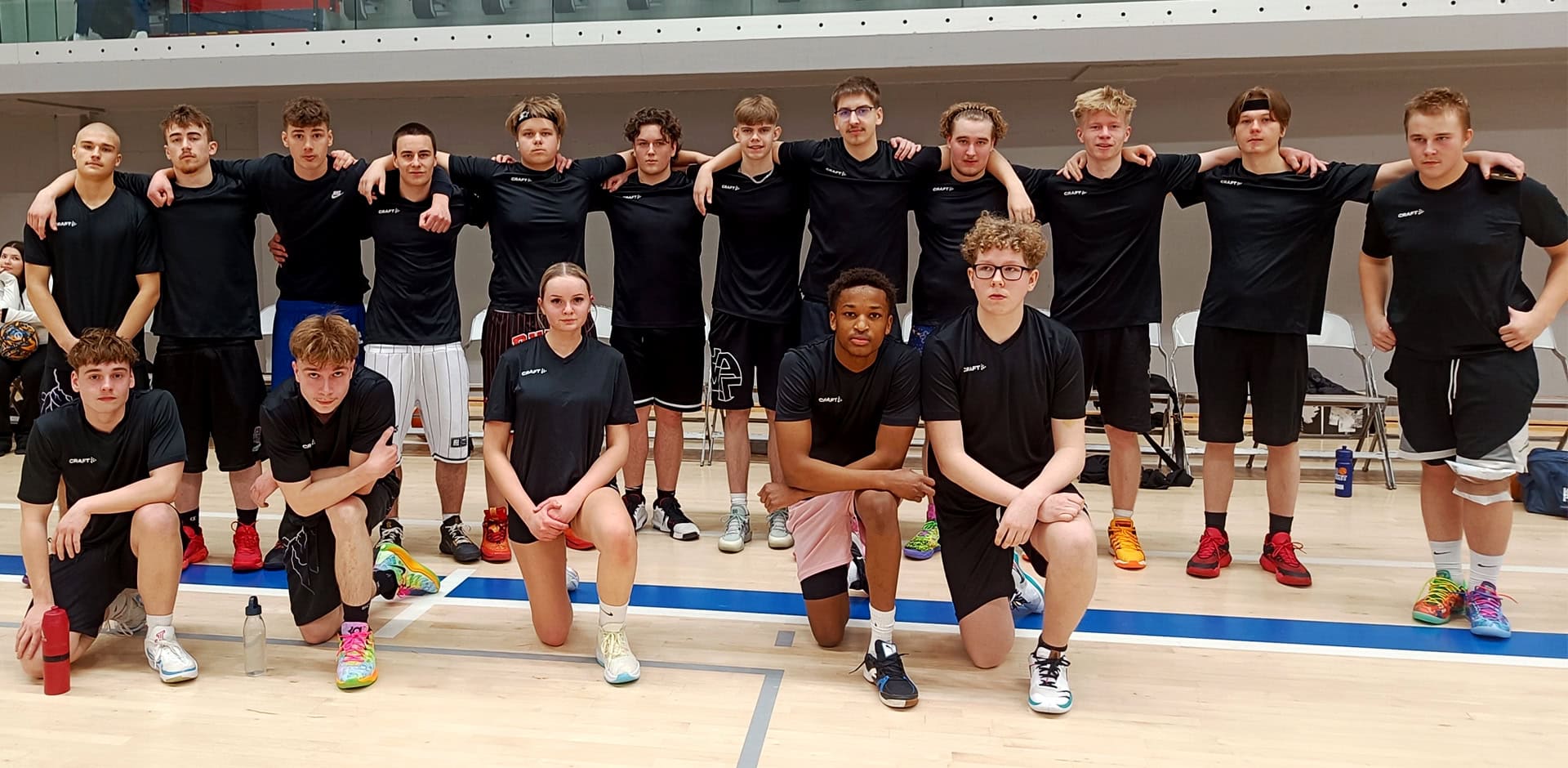 Joukko ihmisiä mustissa pelipaidoissa koripallokentän laidalla.