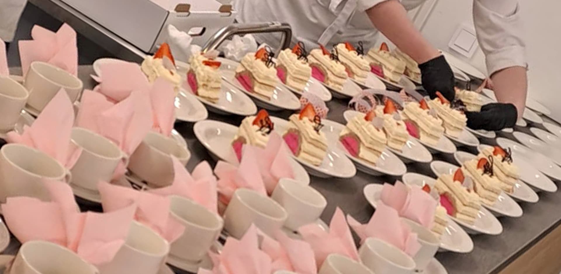 Kakun paloja ja valkoisia kahvikuppeja, joissa vaaleanpunainen servetti.