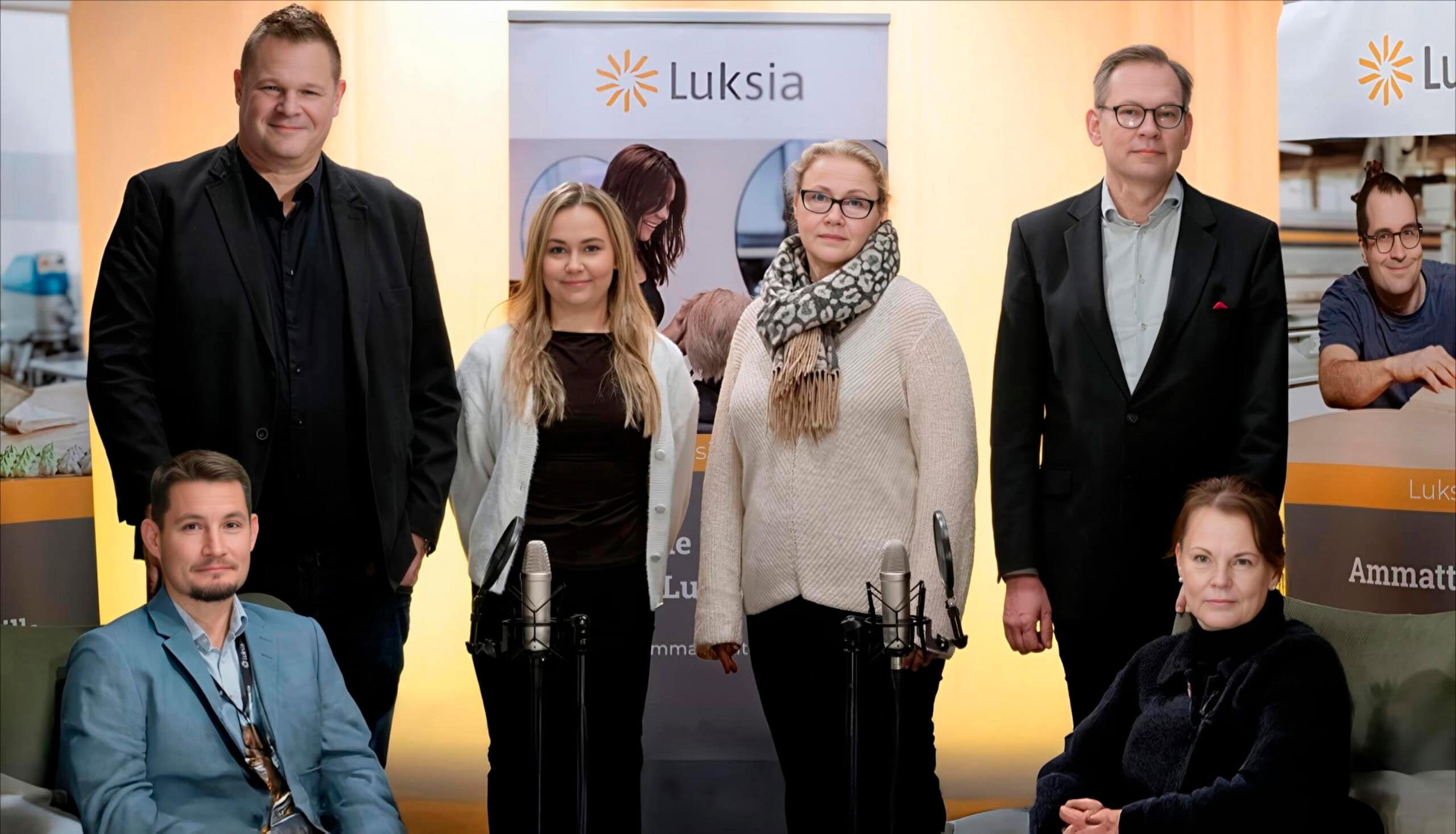 Kuvassa kuusi ihmistä. He seisovat kuvausstudiossa, joka on sävyltään keltainen.